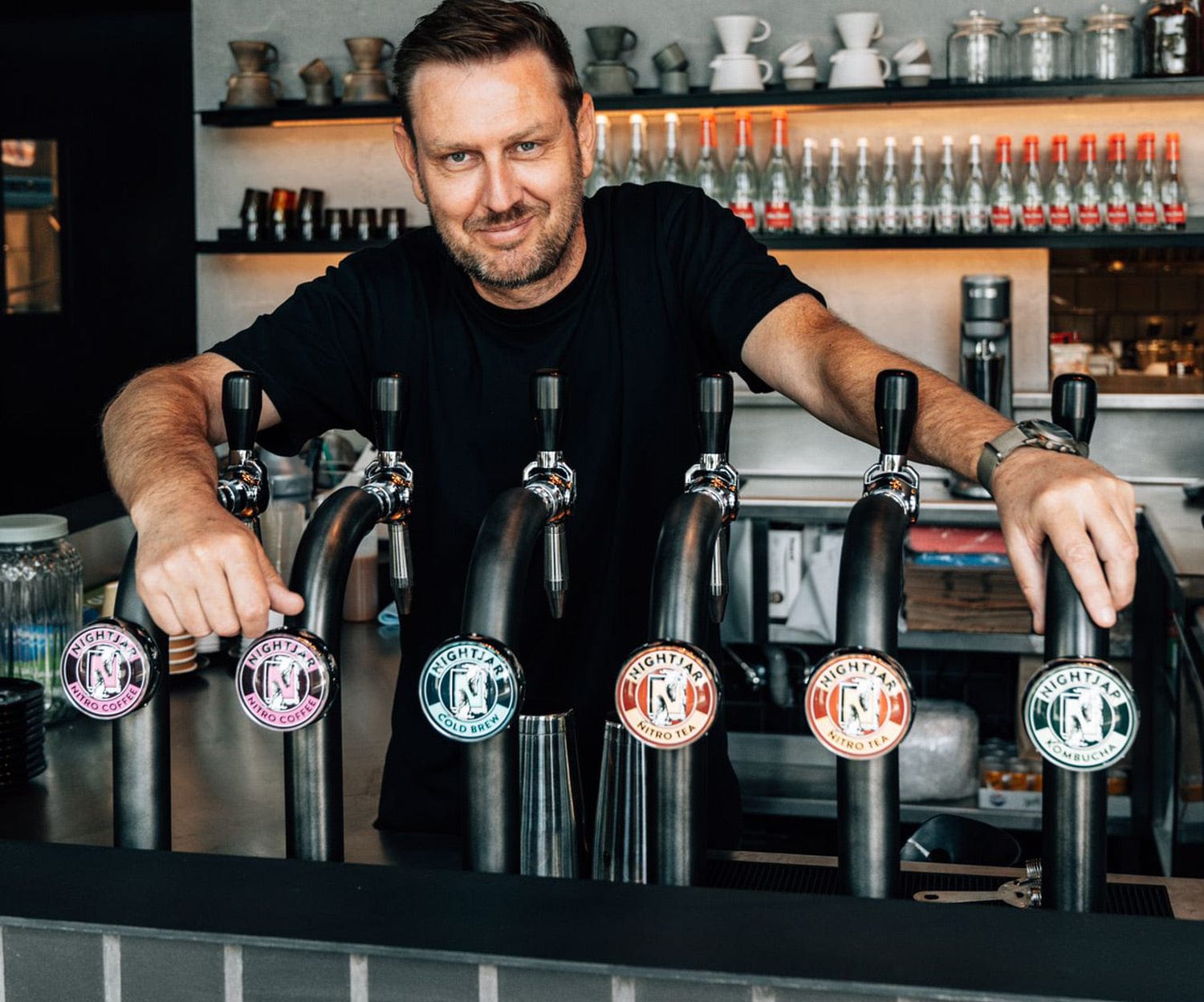 A man in a black shirt leaning over a row of cold brew taps